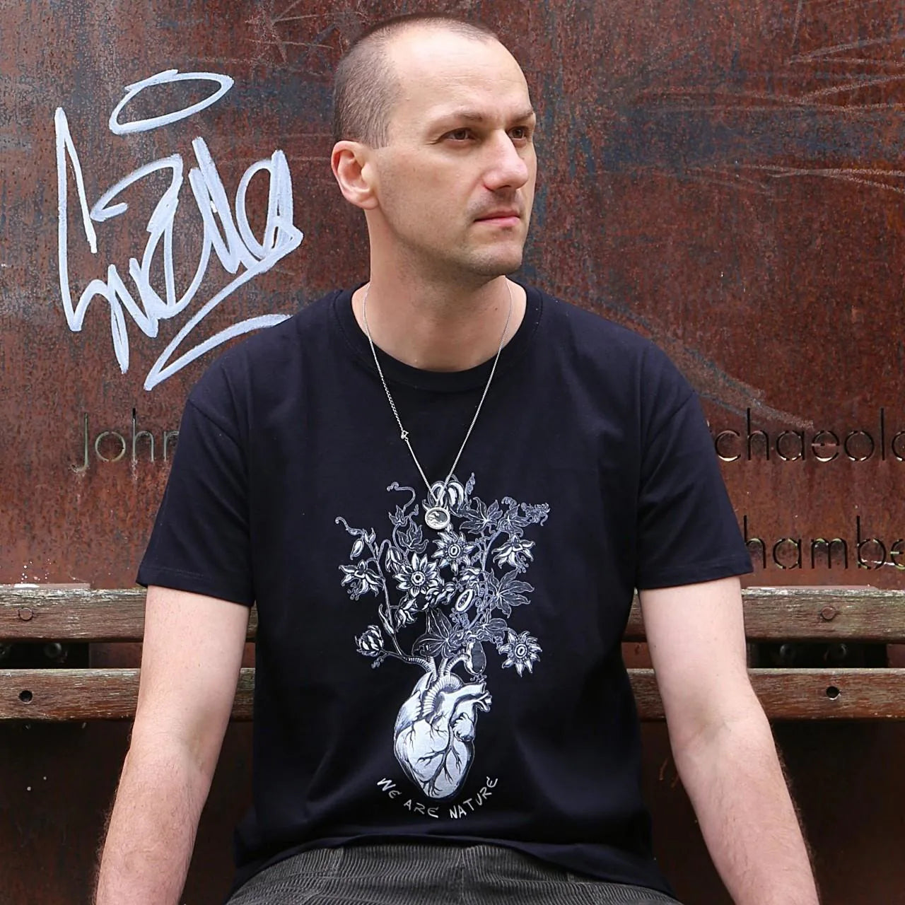 Man wearing a black t-shirt with a floral design sitting on a wooden bench.