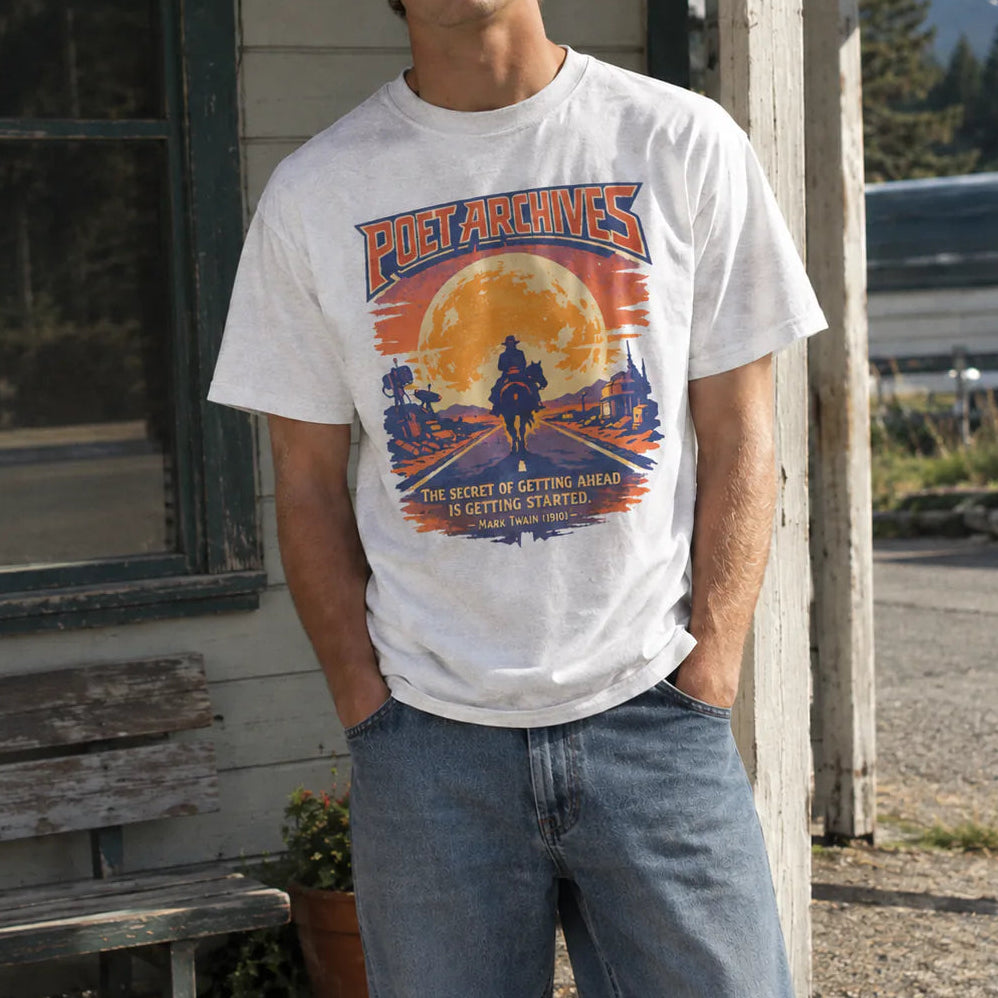 A young man wearing a white graphic t-shirt with a retro sunset design and the text 'POET ARCHIVES', standing outdoors in front of a rustic wooden building.