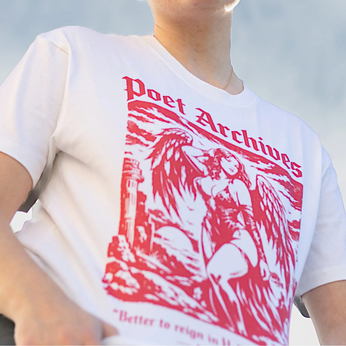 A person outdoors wearing a white graphic T-shirt with a large red 'Poet Archives' print, a black beanie, and sunglasses, photographed from a low angle against a blue sky.