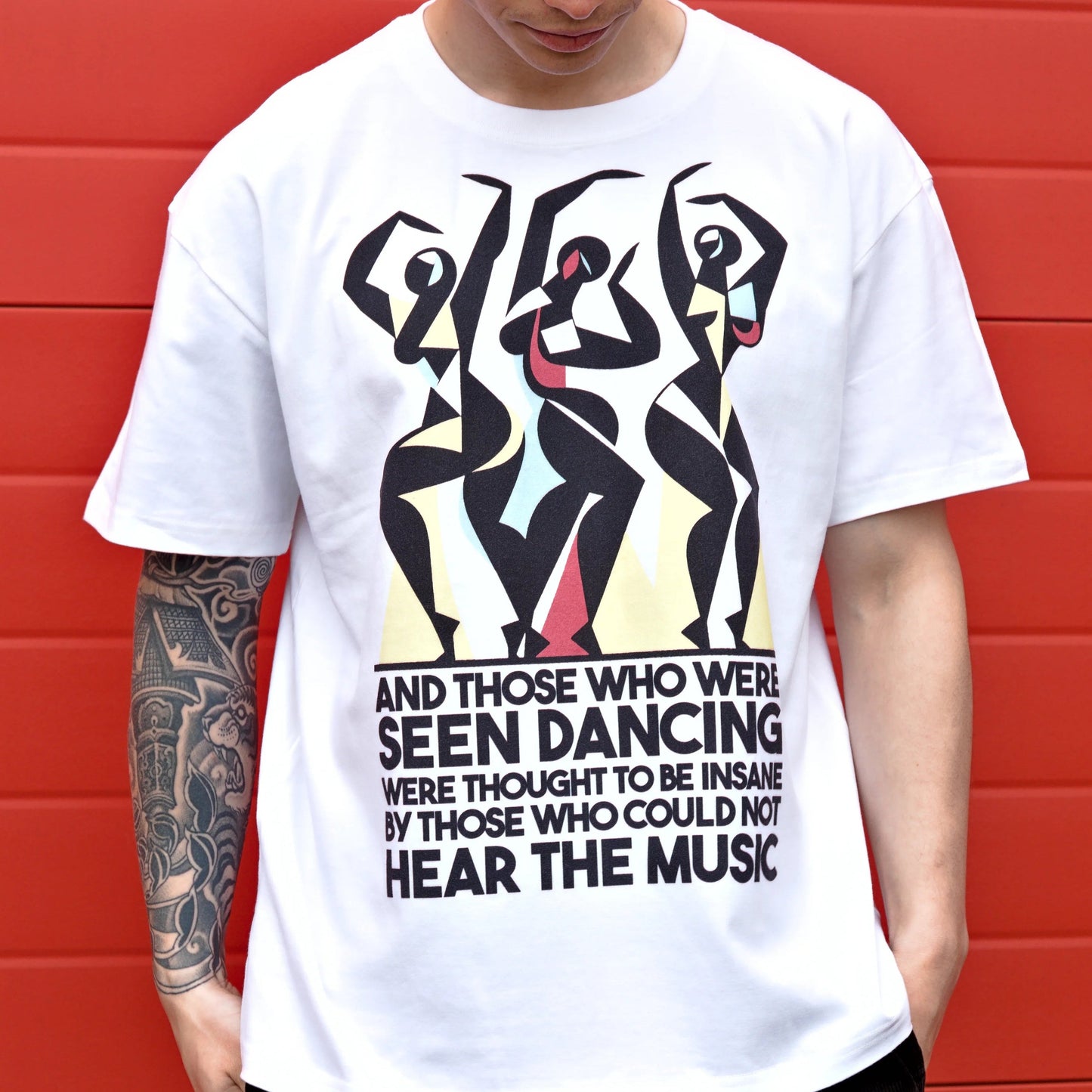 Person wearing a white t-shirt with graphic design and text against a red wall.