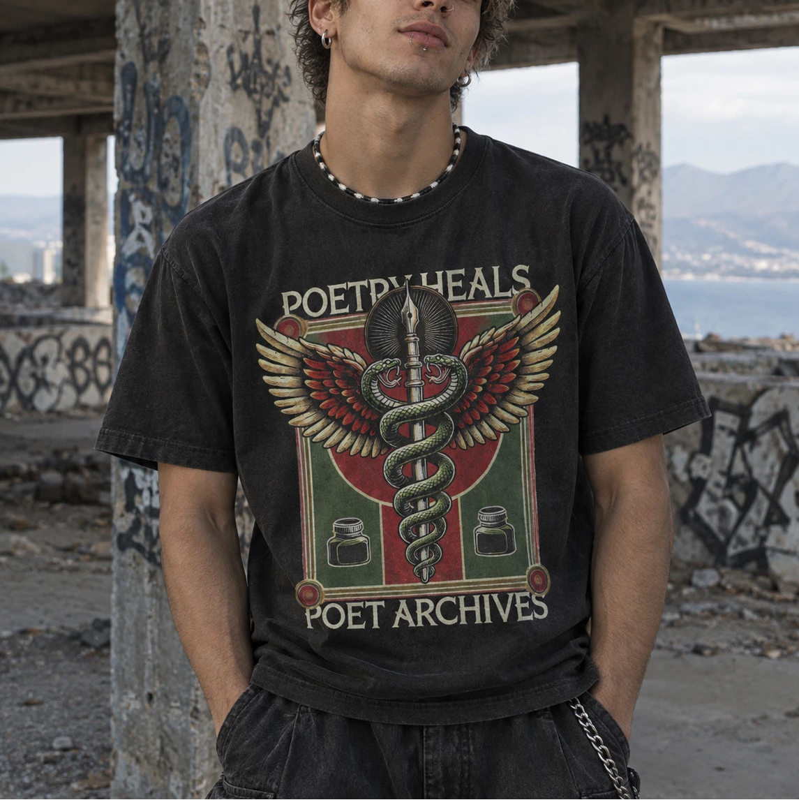 A young man wearing a black graphic t-shirt with a winged snake design and the text 'POETRY HEALS' and 'POET ARCHIVES', standing in a concrete ruin with graffiti.