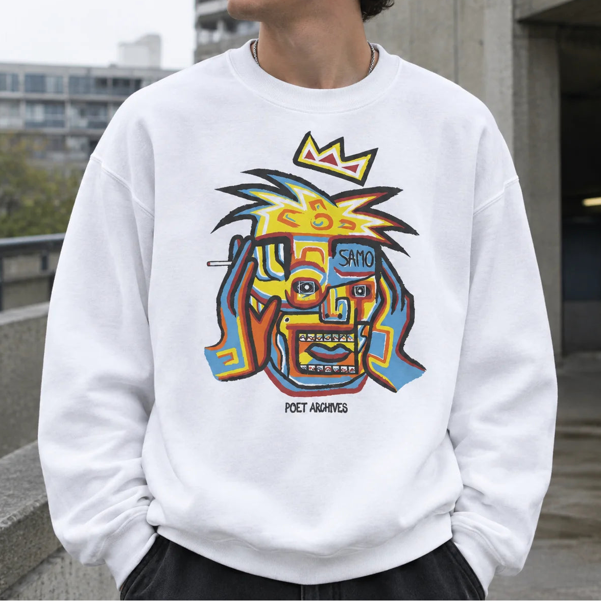A person wearing a white crewneck sweatshirt with a colorful graphic print of a stylized face wearing a crown and the text 'SAMO' and 'POET ARCHIVES'.