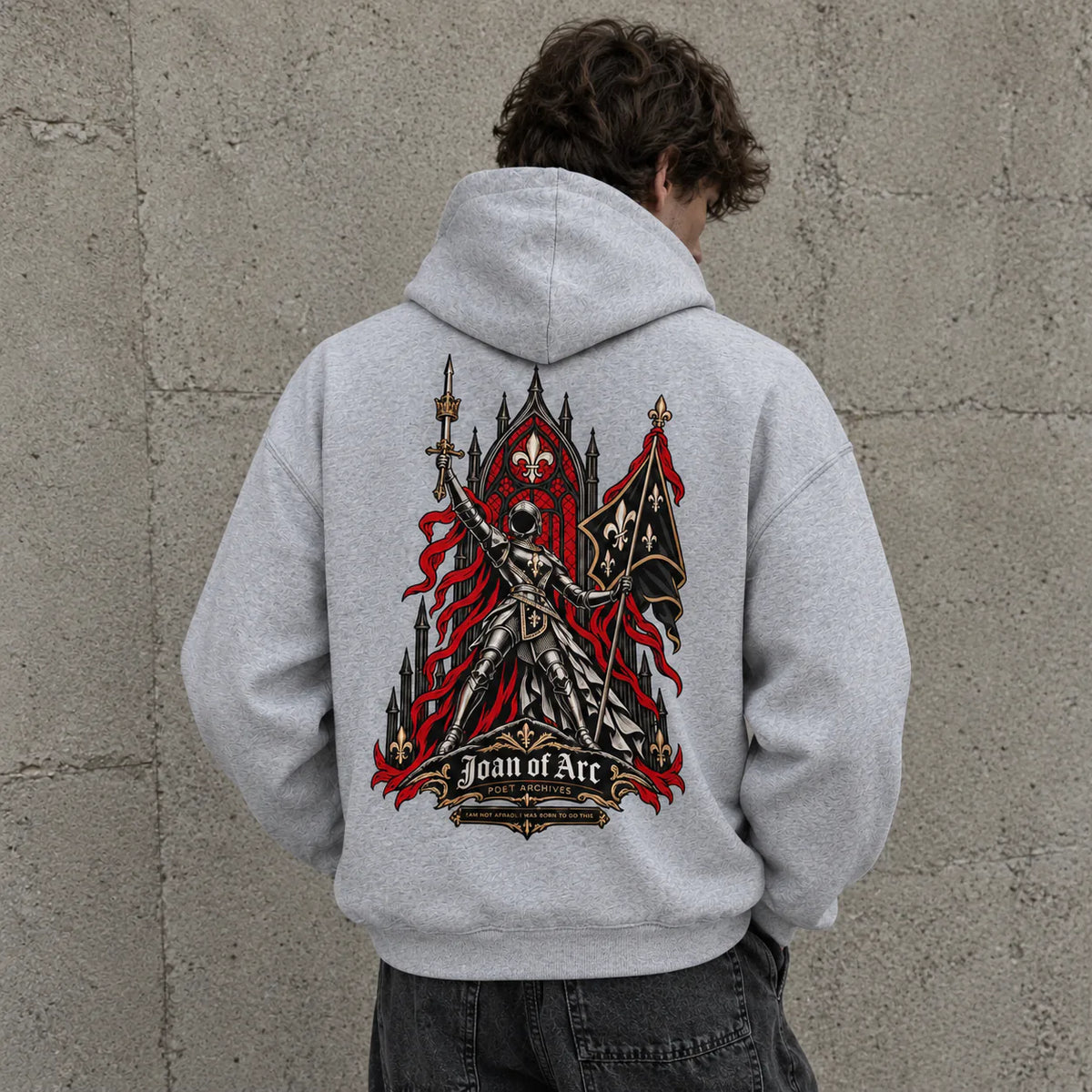 A person viewed from behind wearing a light gray hoodie with a large gothic knight graphic on the back, standing against a textured concrete wall.