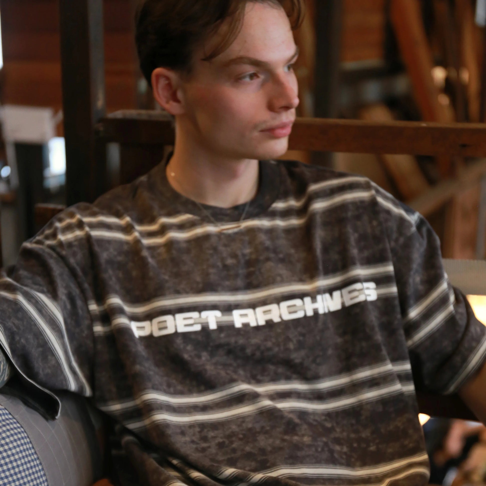 Person wearing a striped shirt with 'Gret Archives' text sitting indoors.