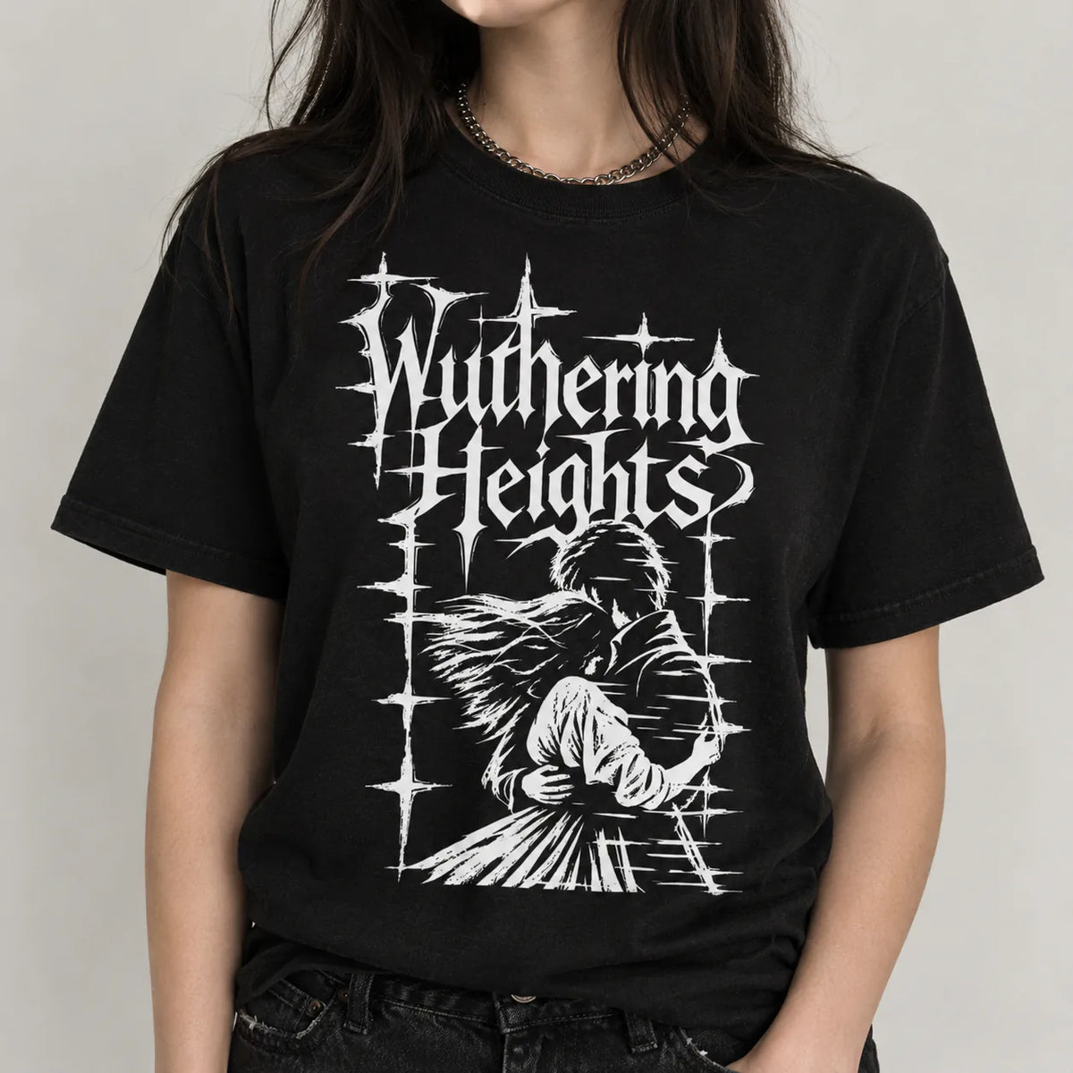 A person wearing a black short-sleeve graphic T-shirt with a large white gothic-style print reading 'Wuthering Heights' and an illustrated figure, photographed against a plain light gray background.
