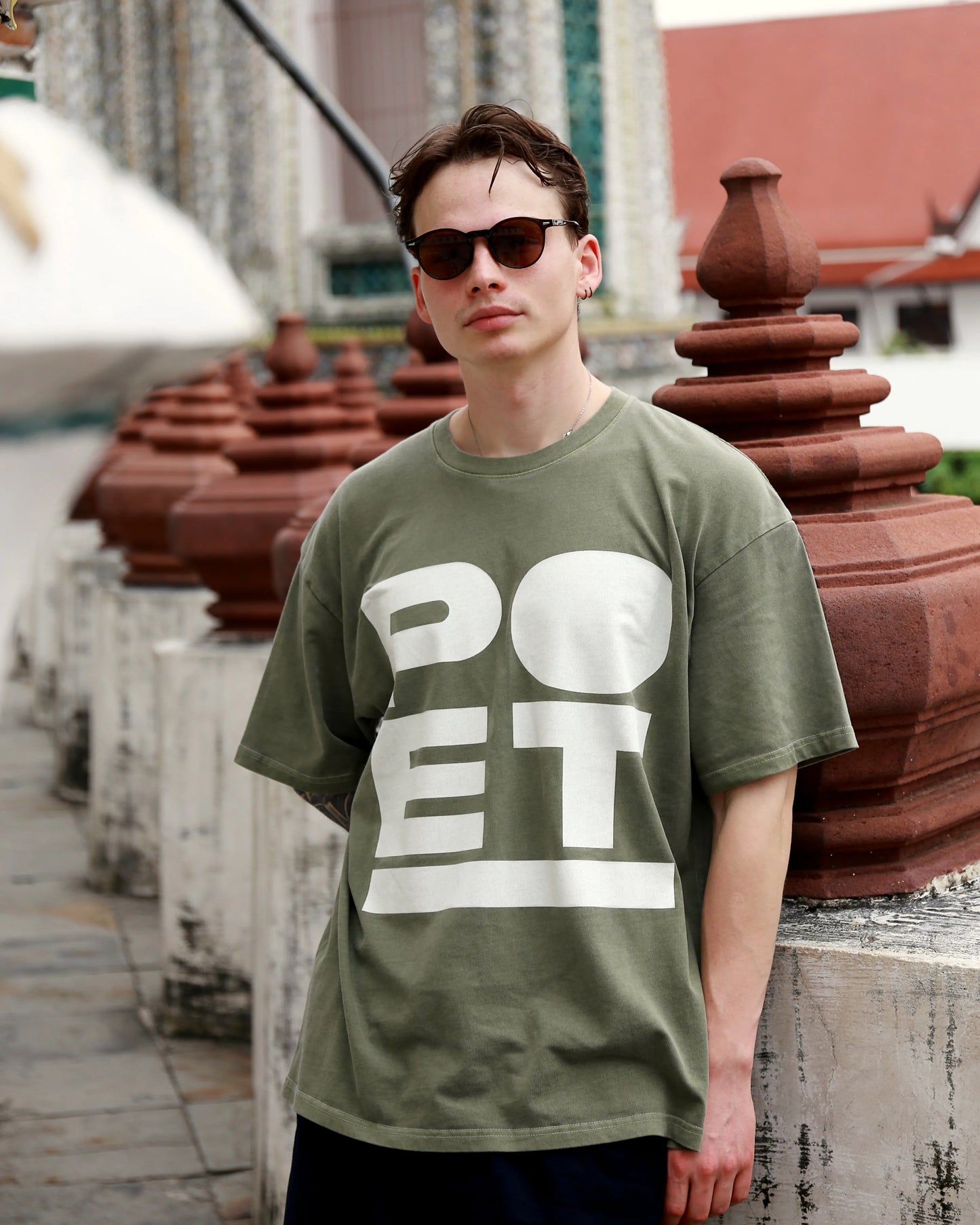 Person wearing a green t-shirt with 'POET' printed on it, standing in front of decorative pots.