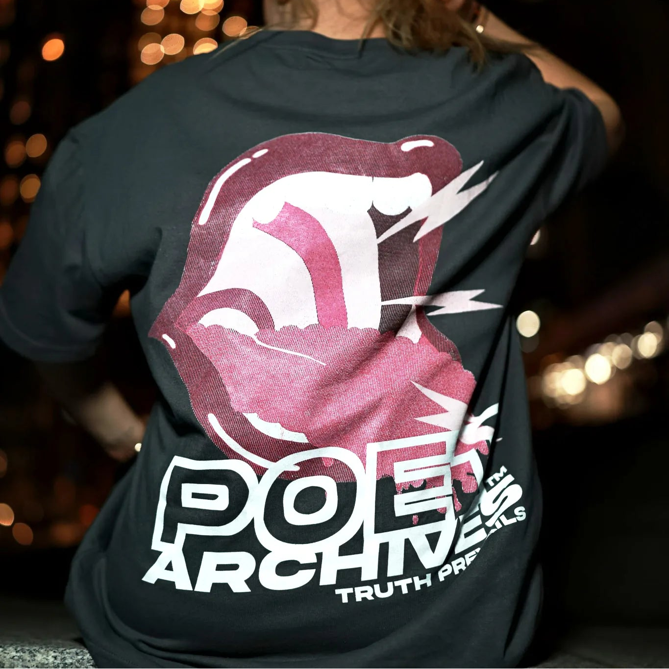 Person wearing a black t-shirt with a graphic design and text on the back, standing against a blurred background.