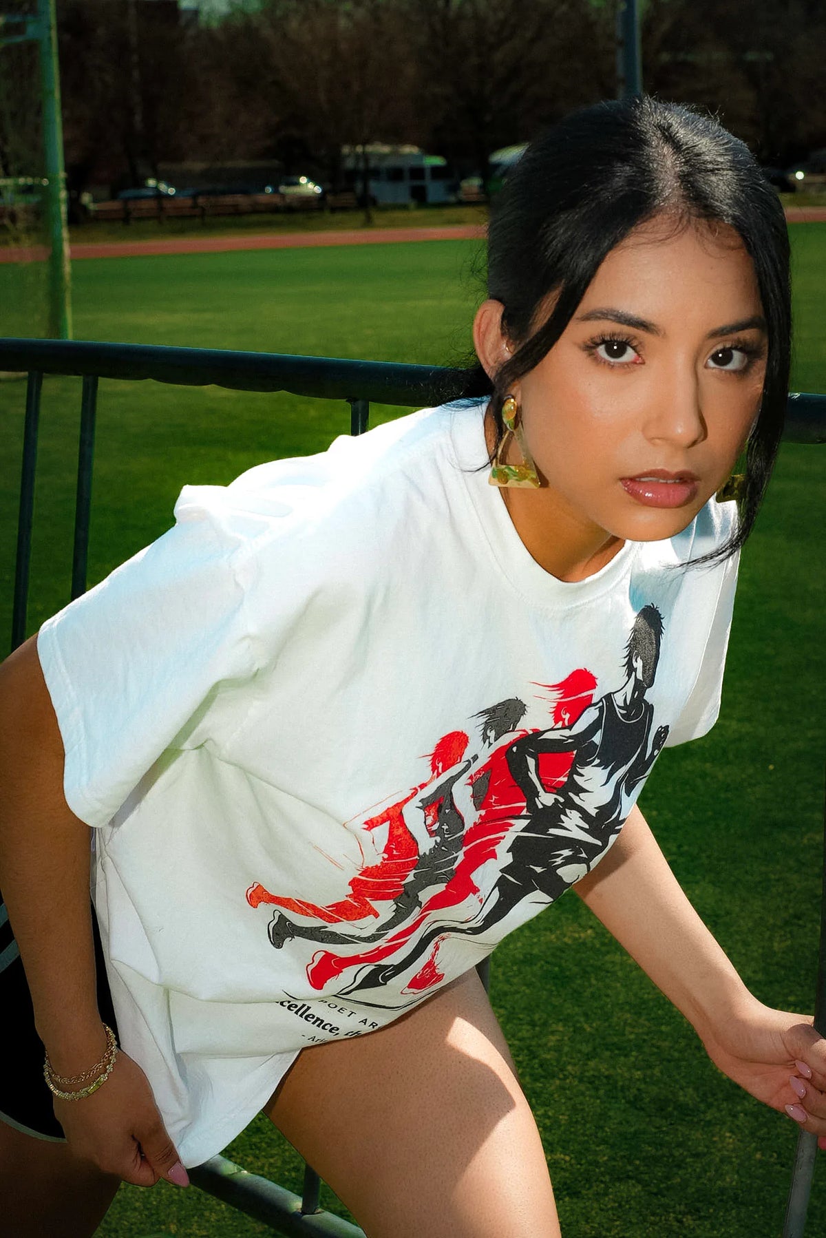 A woman wearing a white oversized graphic t-shirt with a red and black print, photographed outdoors on a grassy field.