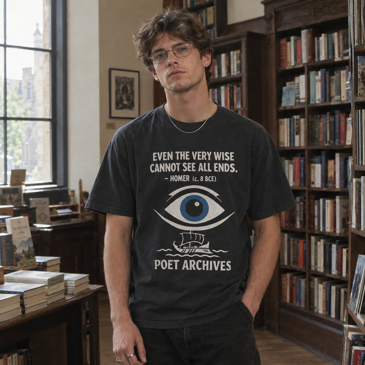 A man wearing a black graphic t-shirt with a white text quote by Homer and a blue eye illustration, standing in a book-filled library.