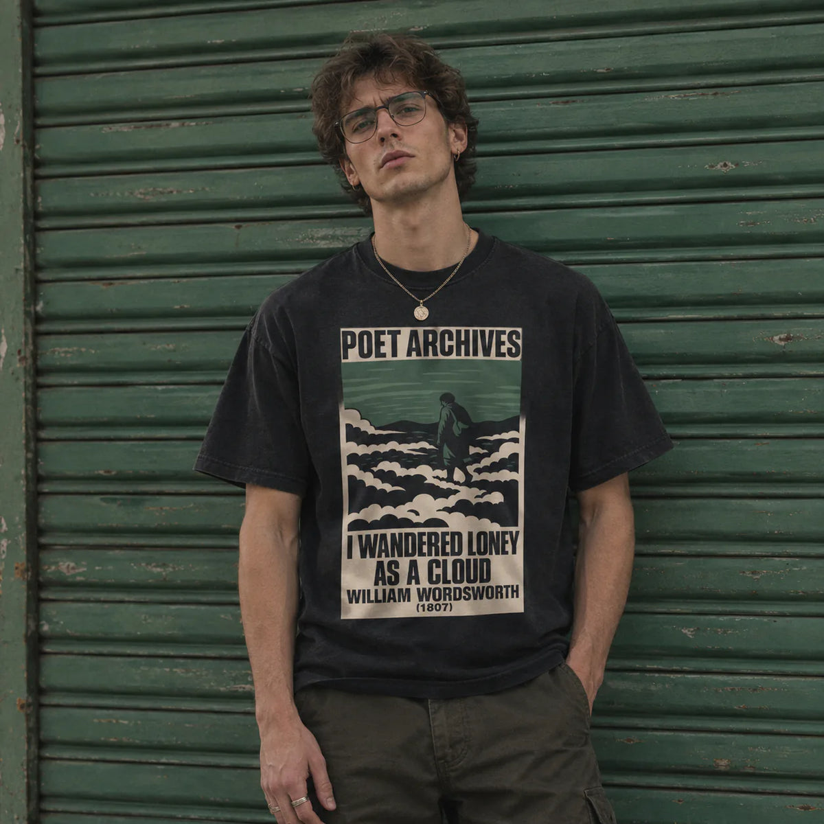 A man wearing a faded black graphic t-shirt with a vintage-style print that reads 'POET ARCHIVES' and 'I WANDERED LONELY AS A CLOUD' attributed to William Wordsworth, standing in front of a green corrugated metal shutter.