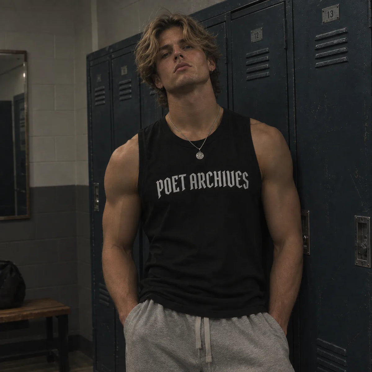 A muscular man with blonde hair stands in a school locker room wearing a black sleeveless tank top with 'POET ARCHIVES' printed in white across the chest, paired with gray sweatpants.