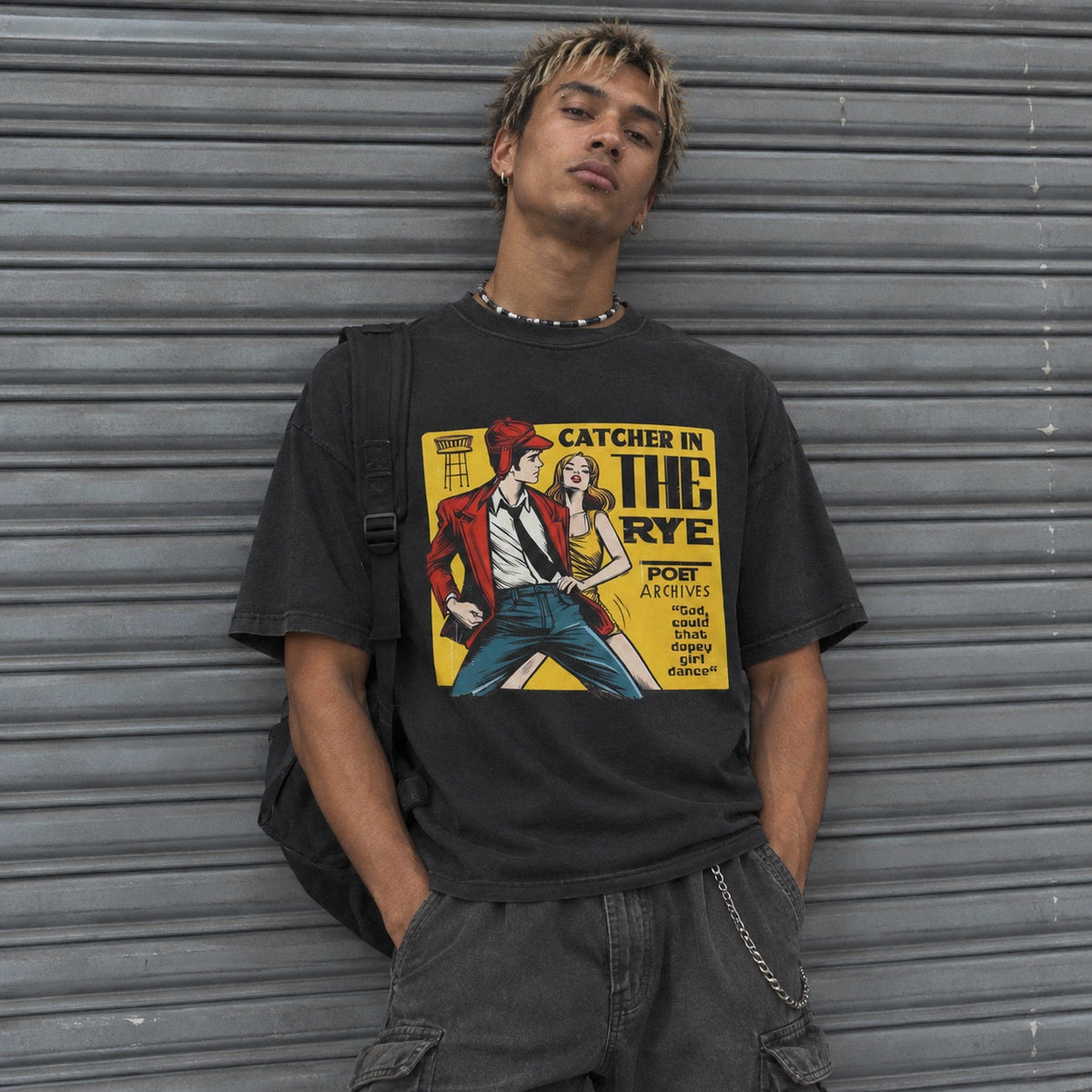 A young man wearing a black graphic t-shirt with a vintage comic-style illustration of a couple in front of a gray metal shutter door.