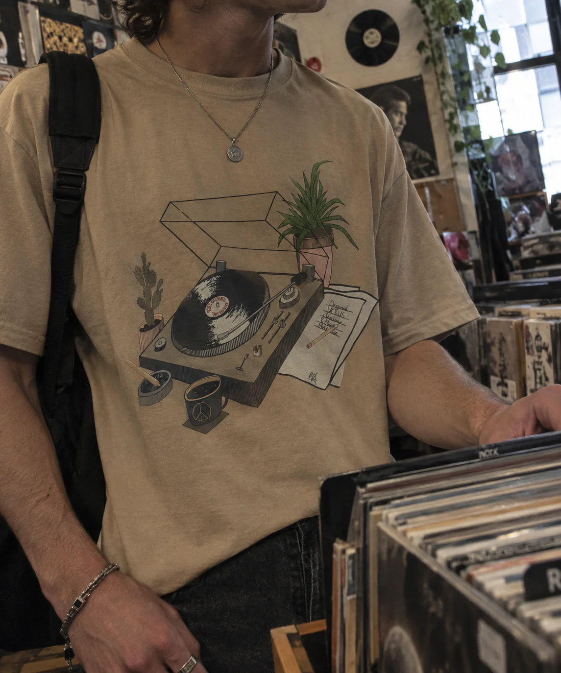 Man wearing a beige Poet Archives t-shirt with a vinyl turntable illustration, browsing records in a record store