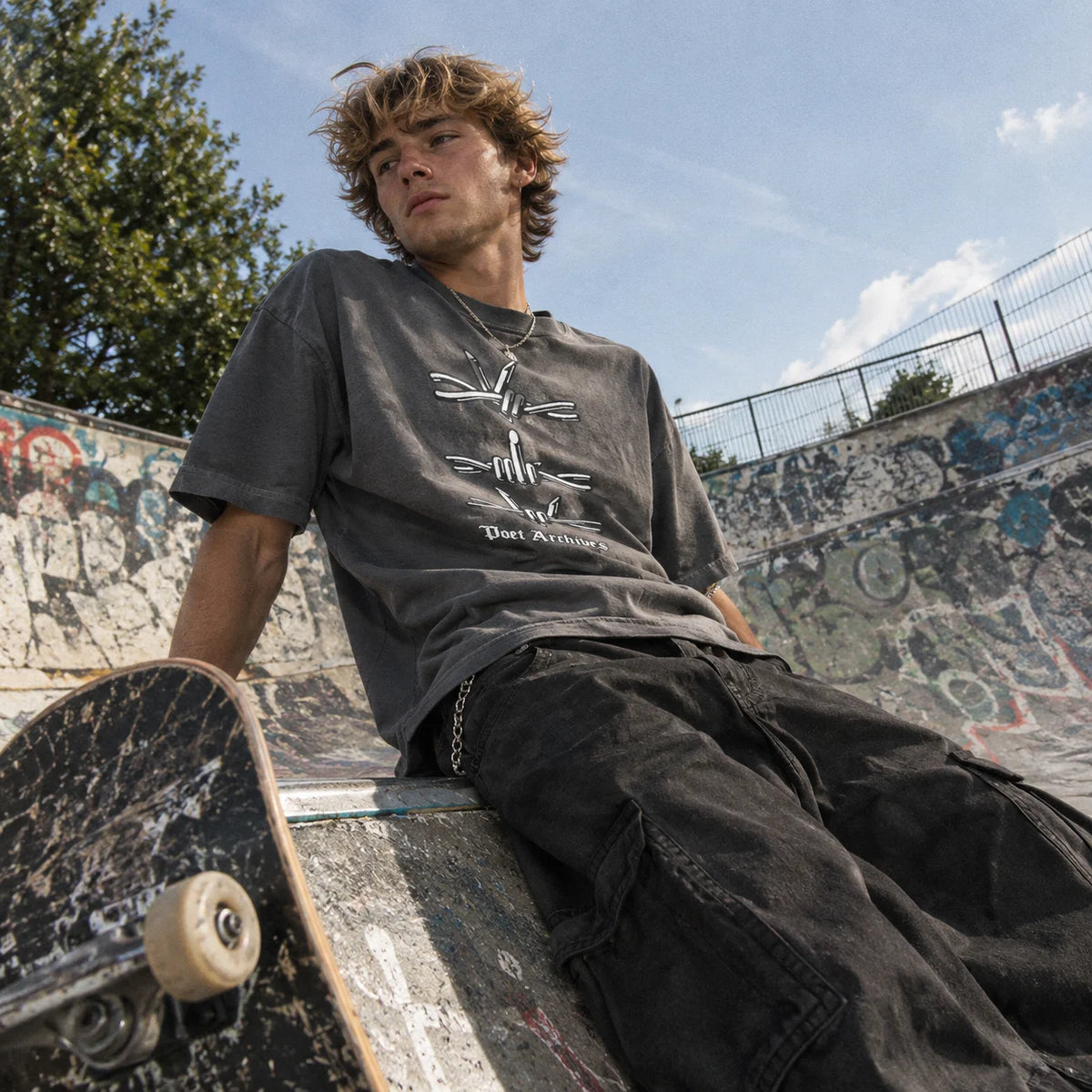 Man at a skatepark wearing a faded black t-shirt with a barbed-wire hand-gesture graphic and 'Poet Archives' text