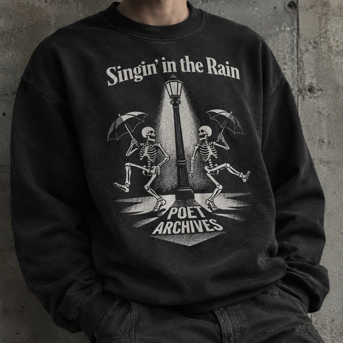 A person wearing a black crewneck sweatshirt with a vintage-style graphic print of two skeletons dancing under a streetlamp with umbrellas, with the text 'Singin' in the Rain' and 'Poet Archives'.