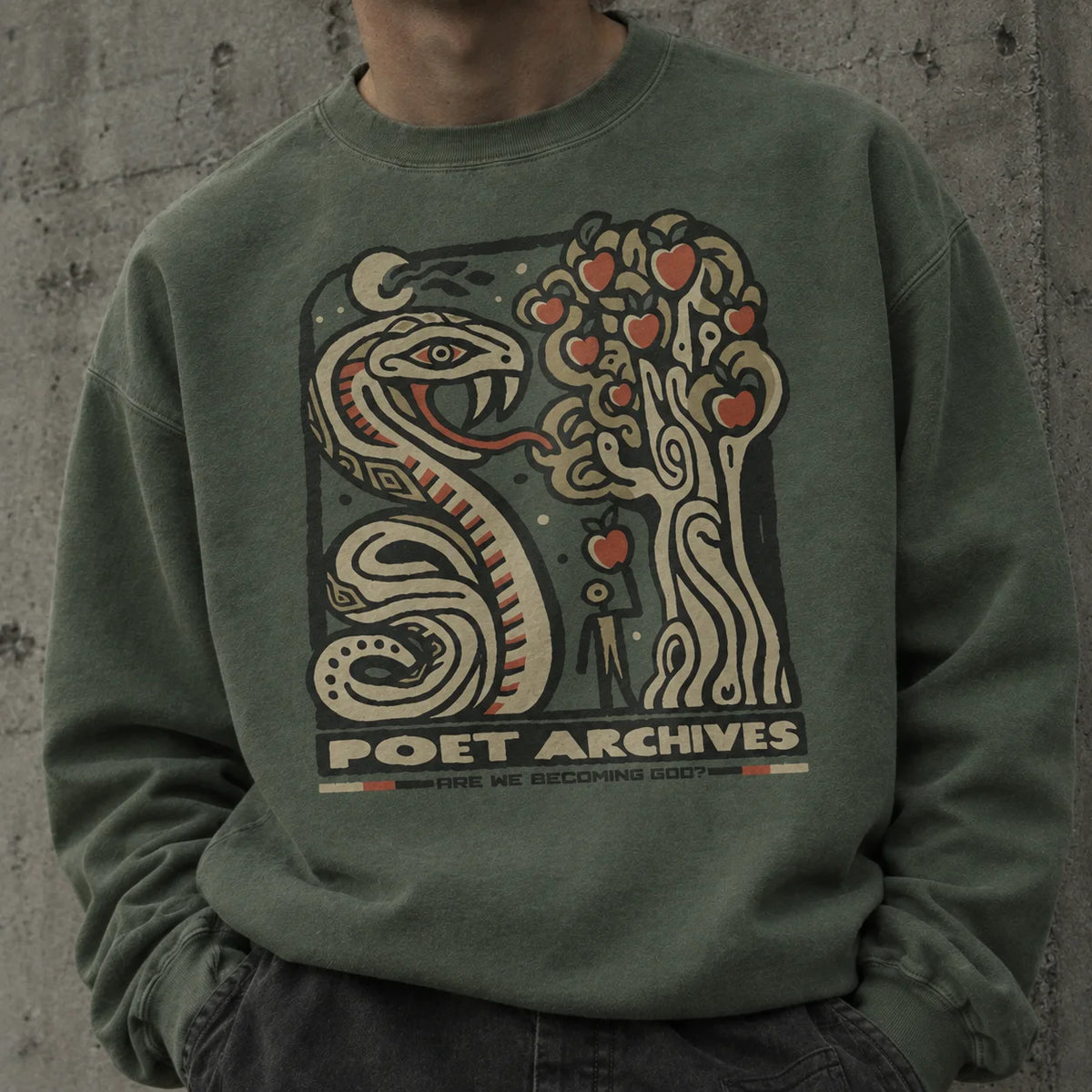 A person wearing an olive green crewneck sweatshirt with a large graphic print featuring a snake, a tree with red hearts, and the text 'POET ARCHIVES ARE WE BECOMING GOD'.