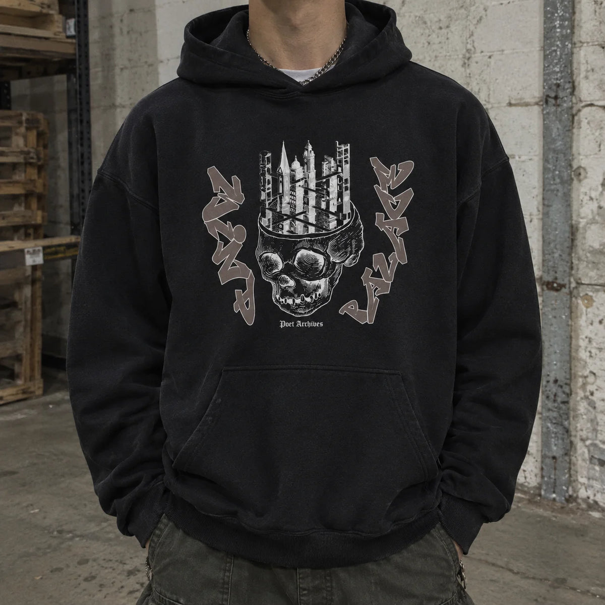 A person wearing a black pullover hoodie with a large front graphic of a skull topped with candles and the text 'Just Ransoms', photographed in an industrial warehouse setting.