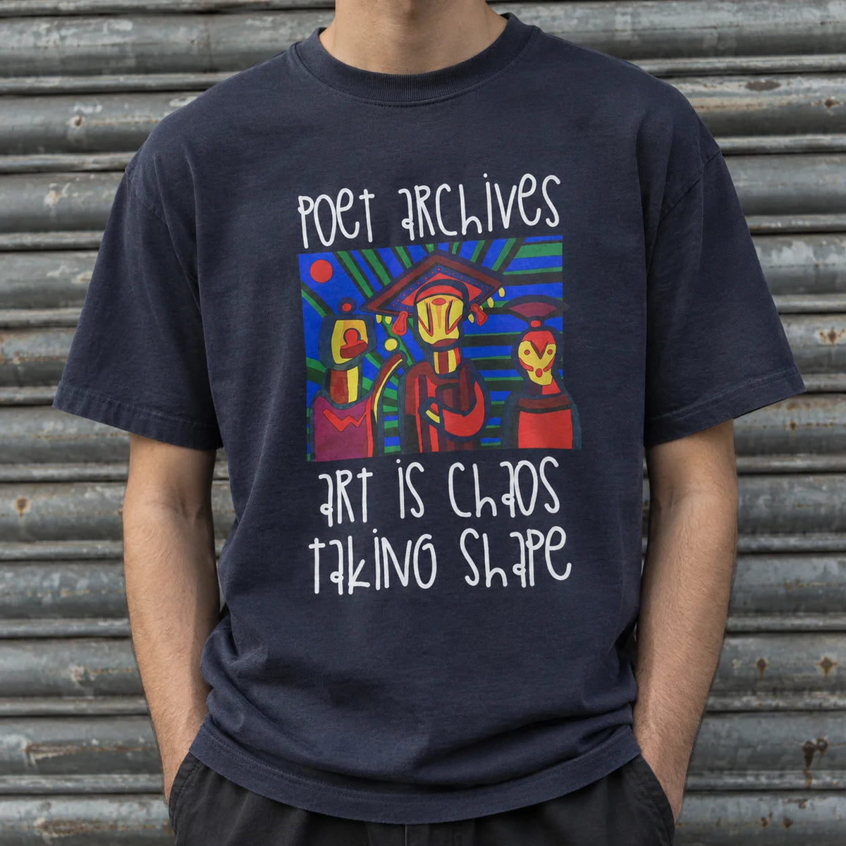 A person wearing a navy blue graphic t-shirt with the text 'poet archives art is chaos taking shape' and a colorful abstract illustration, standing in front of a corrugated metal shutter.