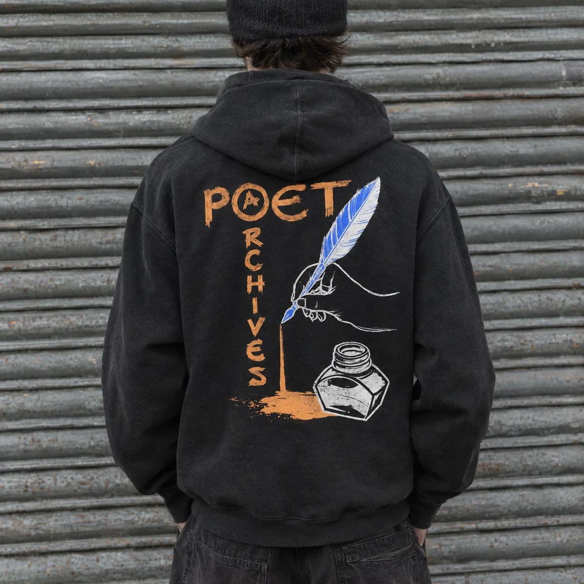 A person viewed from behind wearing a black hoodie with a large graphic on the back. The design reads 'POET ARCHIVES' in orange and white, with a blue-and-white feather quill, white ink bottle, and orange ink splash.