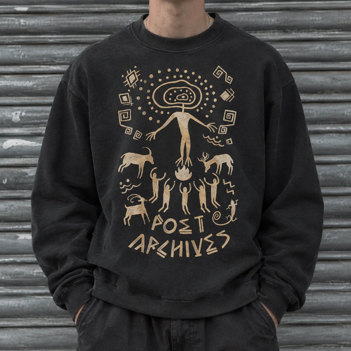 A person wearing a black crewneck sweatshirt with a beige graphic print on the front. The graphic features a stylized figure, animals, and the text 'POET ARCHIVES'.