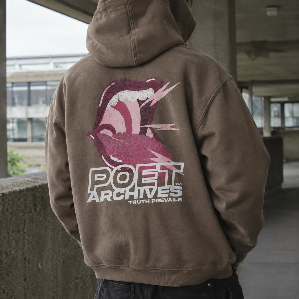 A person wearing a brown pullover hoodie with a large graphic on the back, standing in an outdoor concrete walkway. The hoodie features a pink and white roaring mouth logo above the text 'POET ARCHIVES' and 'TRUTH PREVAILS'.
