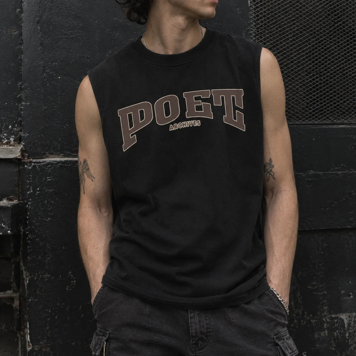 A man wearing a black sleeveless muscle tank top with 'POET' and 'ARCHIVES' printed in brown varsity-style lettering on the chest, posed against a dark textured wall.