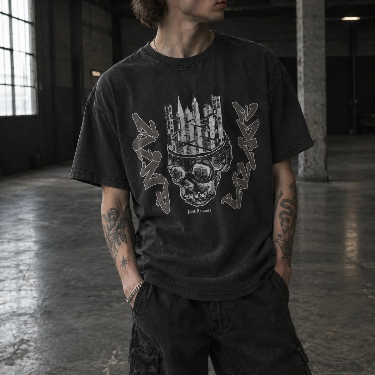 A person wearing a washed black graphic t-shirt with a skull and cityscape design, standing in a dark industrial loft space.