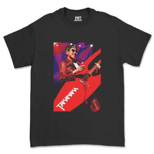 A black short-sleeve crewneck t-shirt featuring a large graphic print of musician Masayoshi Takanaka playing a red Takada guitar on a stage with purple and pink lighting. The brand name 'Poet Archives' is printed inside the collar.
