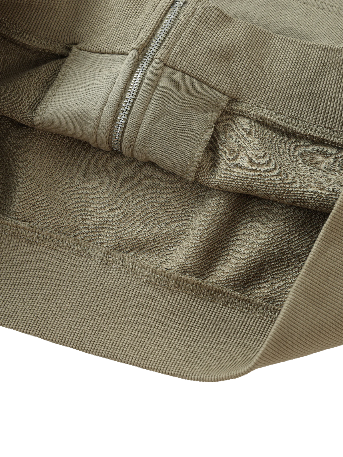 Close-up detail of a ribbed knit garment in a warm taupe-beige color, showing the texture of the fabric, a silver zipper, and a matching fabric pocket.